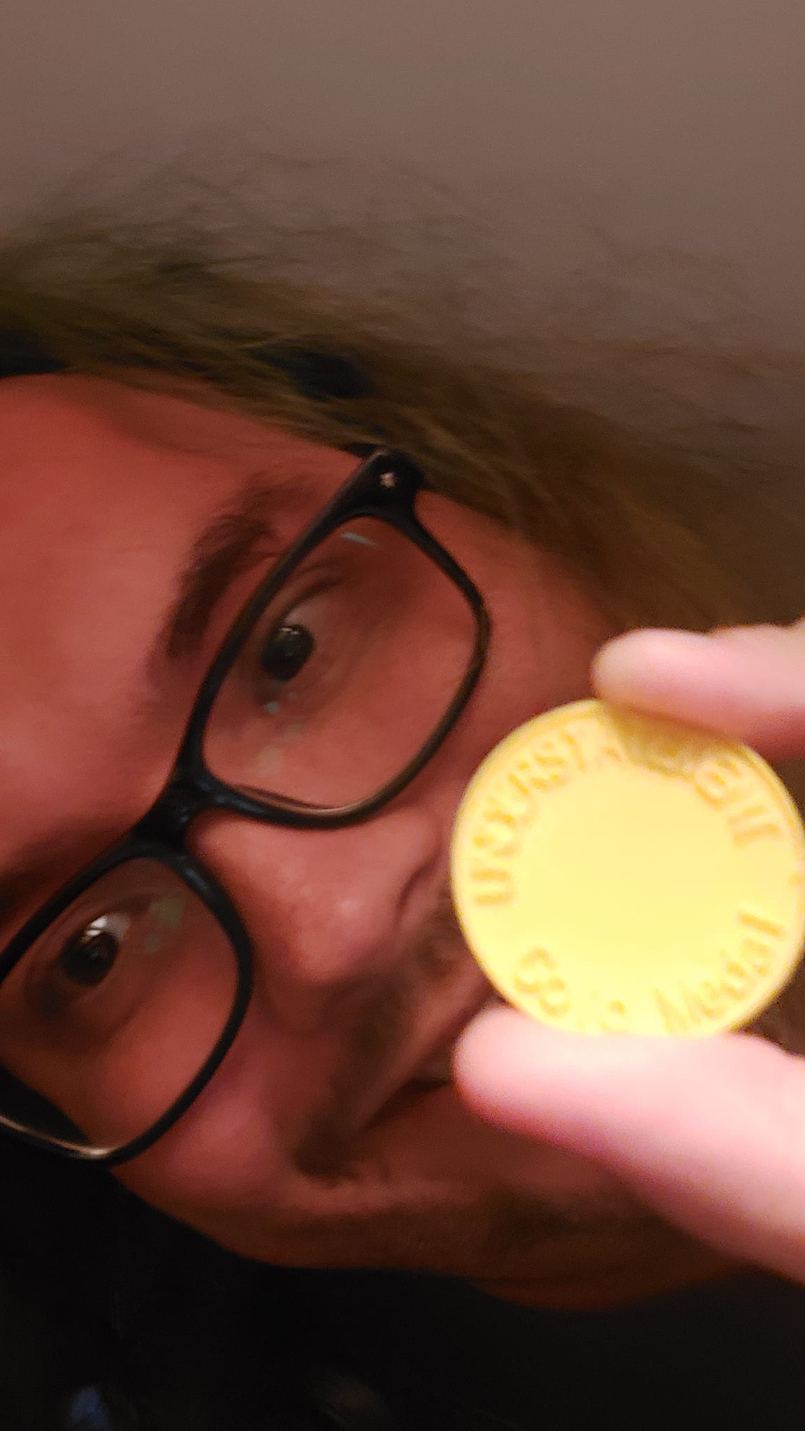 A man with long green hair and no beard holds a plastic coin with text "understatement gold medal"